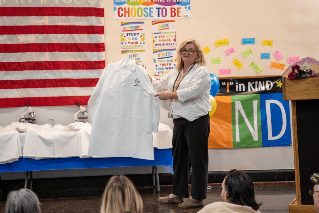 Lake View's Principal Erin McMahon unveils the white lab coats on stage.